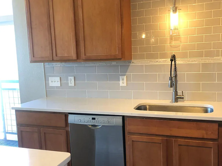 Large single-basin sink and beautiful glass tile backsplash. Also featured are some of the many kitchen cabinets, providing ample storage space