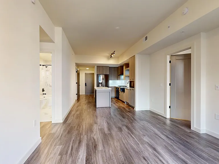 Apartment kitchen with black stainless steel appliances, dining and living room with wood-style flooring.