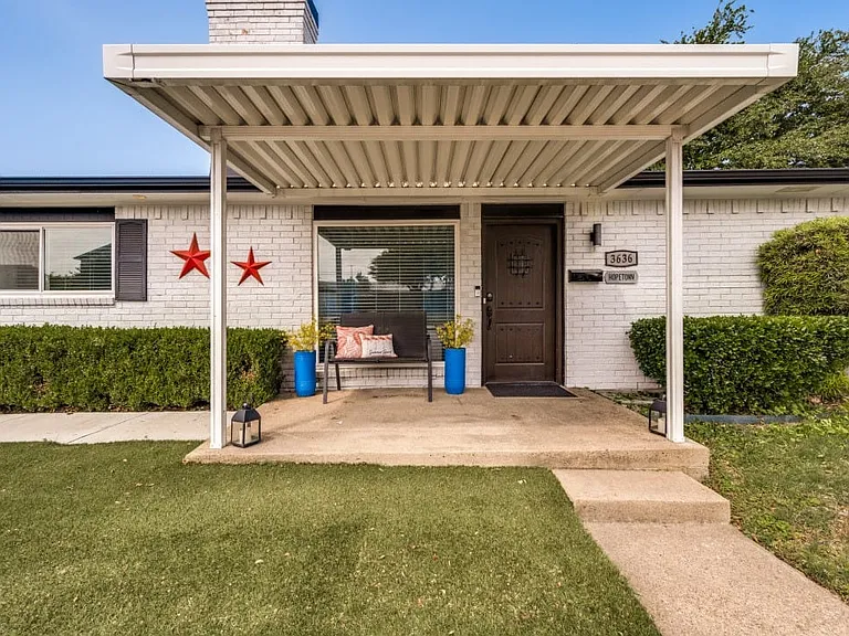 White brick exterior featuring a covered front porch, dark wood-finish entry door, and manicured shrubbery