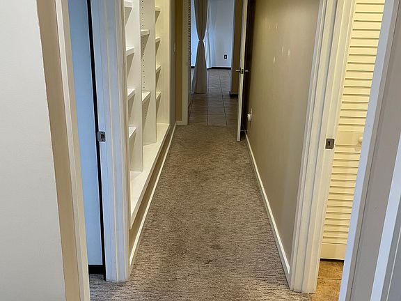 Hallway coming from garage entrance. There's a small mudroom area with a bench and coat hooks (left). Immediate right is secondary bedroom entrance. Next right is bathroom entrance. Primary bedroom is on the left. Built in bookcases.