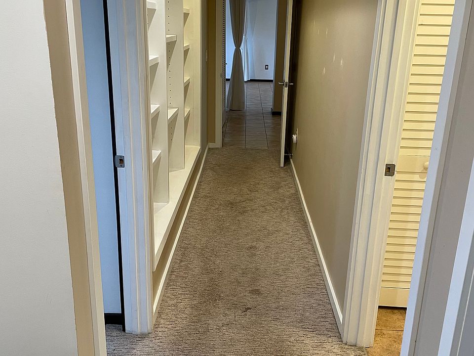 Hallway coming from garage entrance. There's a small mudroom area with a bench and coat hooks (left). Immediate right is secondary bedroom entrance. Next right is bathroom entrance. Primary bedroom is on the left. Built in bookcases.