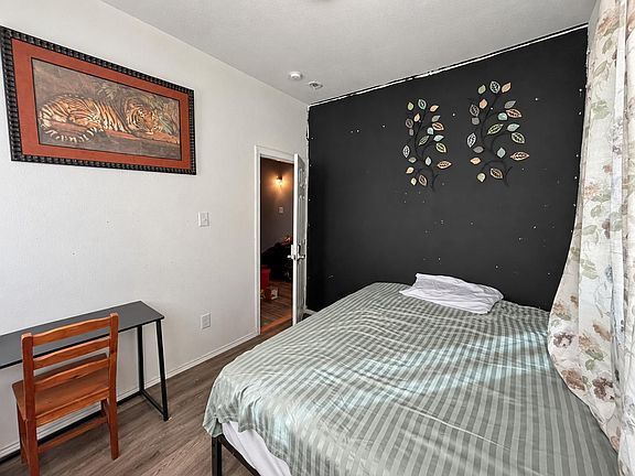 Private bedroom with full-size bed, work desk, and wood-look flooring, plus window coverage for added privacy.
