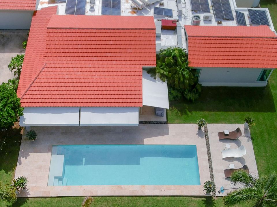 Aerial view of the pool area with a spacious green yard, perfect for family gatherings and relaxation. The property features a concrete roof and solar panels, offering energy efficiency and comfort in a private and elegant setting