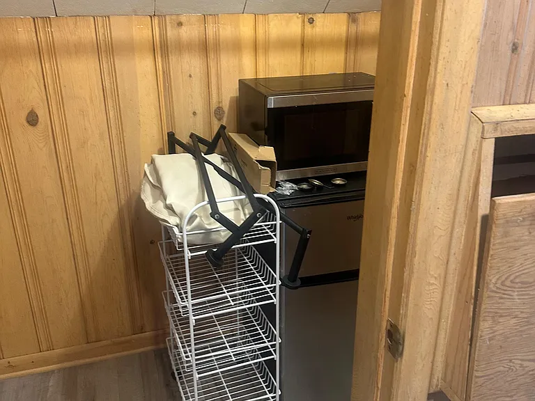 Compact kitchenette nook with wood paneling, vinyl flooring, and space for a mini fridge, microwave, and storage cart.