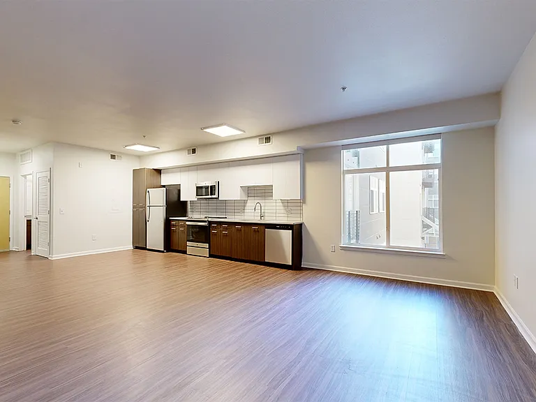 Apartment kitchen with stainless steel appliances, dining and living room with wood-style flooring.