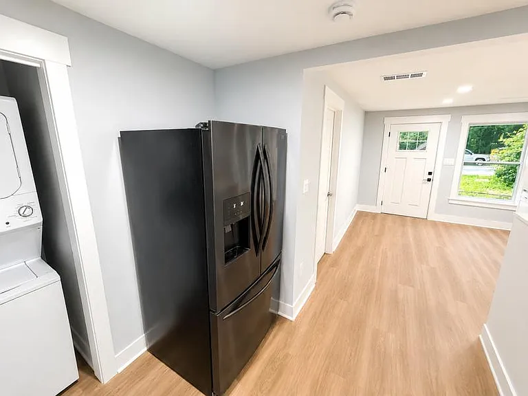 Open-concept entry and kitchen area with wood-look flooring, a French-door refrigerator, and an adjacent laundry closet.