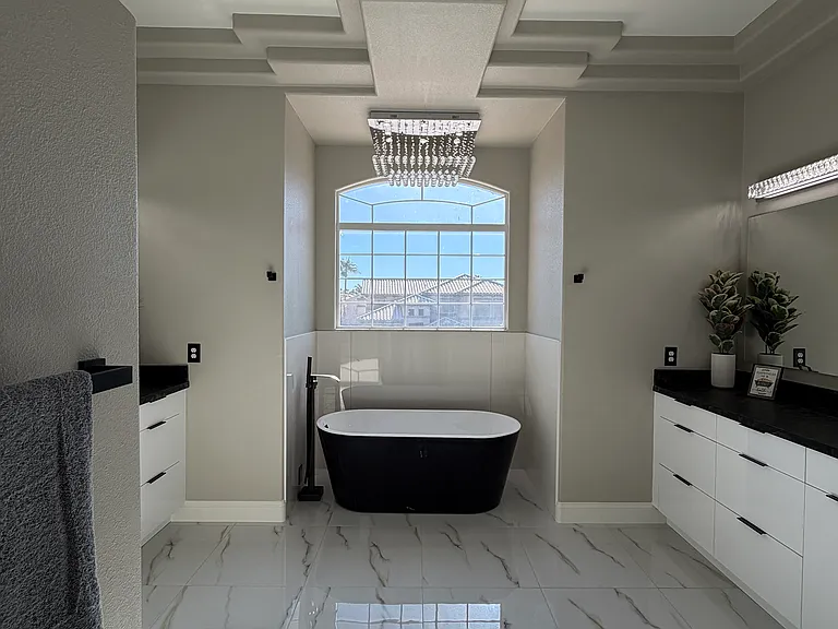 Elegant primary bath featuring a freestanding soaking tub with large picture window and elegant overhead lighting