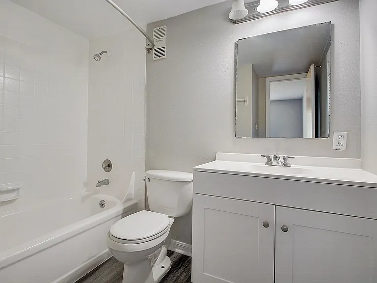 Modern bathroom with sleek white fixtures, featuring a spacious bathtub, elegant vanity, and large mirror, offering a bright and inviting atmosphere.