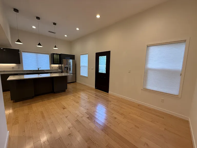 Spacious living room adjacent to the kitchen featuring hardwood flooring throughout with recessed lighting, and multiple windows filling the space with natural light.