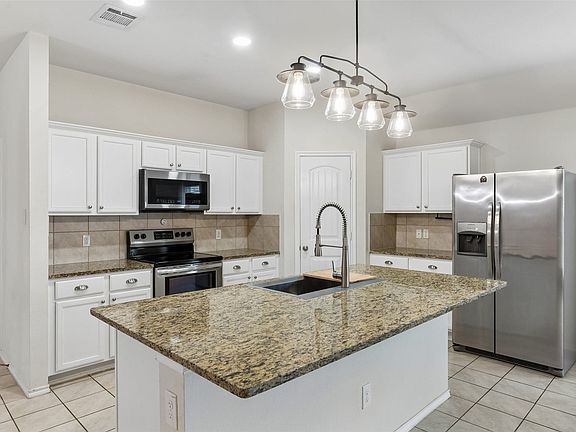 Kitchen featuring a central island with an undermount sink, granite countertops, and white cabinetry