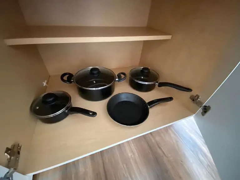 Kitchen cabinet stocked with pots, pans, and matching lids for cooking convenience.