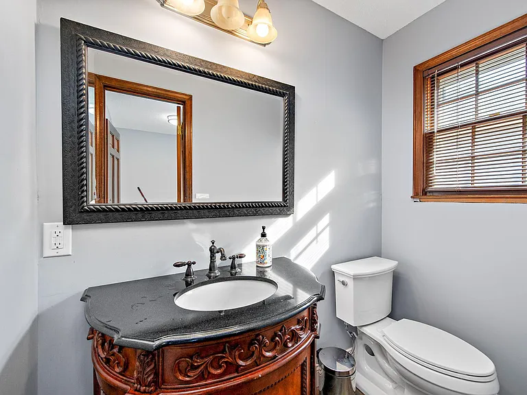 Bathroom vanity area features a stone-look countertop, oil-rubbed bronze fixtures, and a large framed mirror with window blin