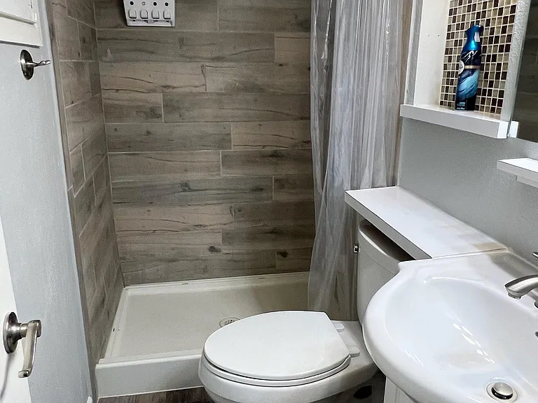 Bathroom with a tub/shower combo, tile surround, vanity with storage, and built-in shelving for toiletries.