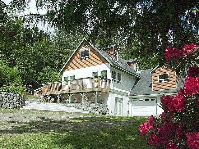 Front with lower parking and attached garage. Concrete patio leads up to deck