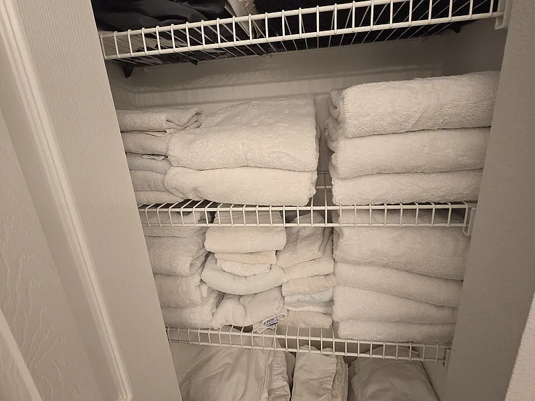 Large walk-in closet stocked with linens, towels, blankets, luggage cart, and roll-in portable bed for guests