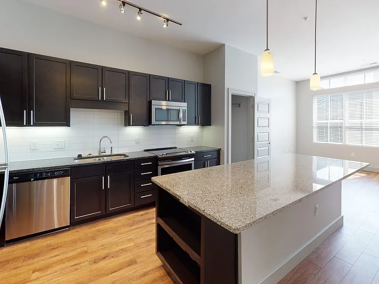 Apartment kitchen with stainless steel appliances, granite countertops and wood-style flooring.