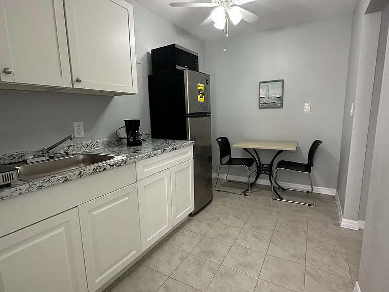 Eat-in kitchen with ample white cabinetry, granite-look counters, stainless fridge, and a small dining nook.