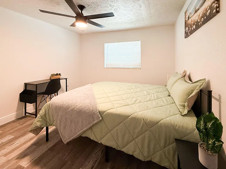Spacious furnished bedroom with a ceiling fan, window blinds, and a dedicated desk areaideal for sleep and study.