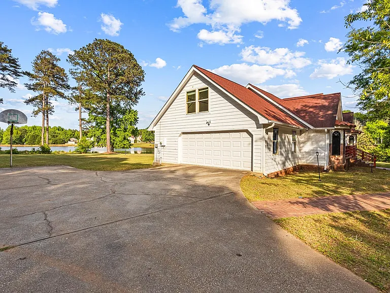 Spacious driveway leads to a two-car garage and side entry, set on a large lawn with mature trees and water views.