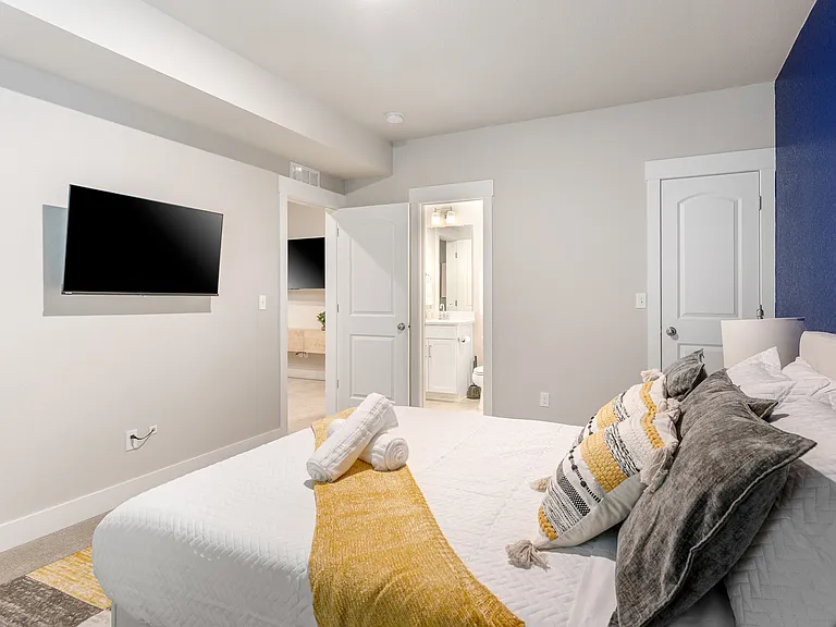 Modern bedroom with a bold navy blue accent wall and soft neutral tones. Features a comfortable bed with decorative pillows and a mustard yellow throw. Includes a wall-mounted TV and an en-suite bathroom, offering convenience and style for your stay.
