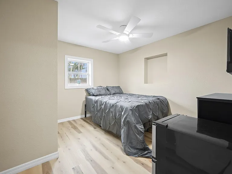 Private bedroom with wood-style flooring, ceiling fan, and a window for natural light, plus space for a TV and dresser.