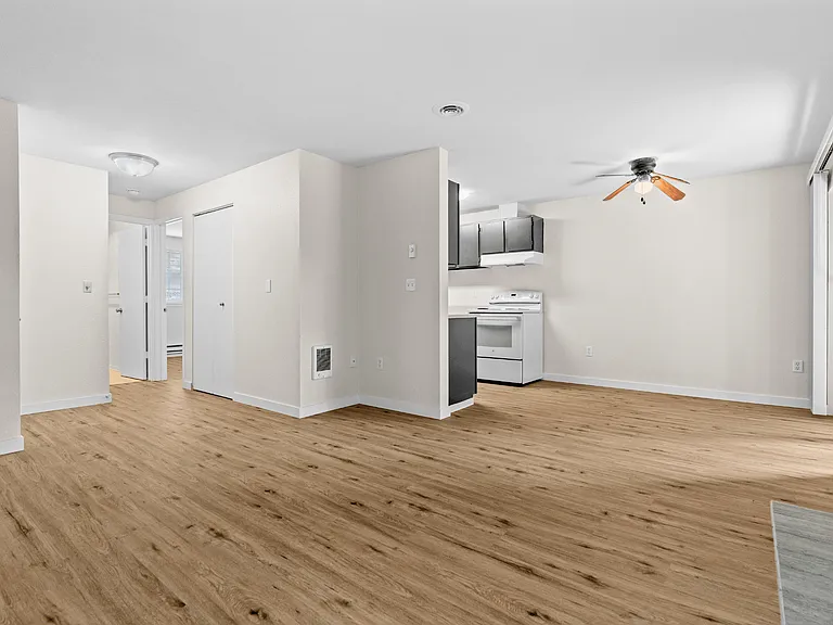 Open-concept living and dining area with wood-style plank flooring, ceiling fan, and open kitchen access at Garden Square Apartments in Lakewood, WA. Open-concept living and dining area with wood-style plank flooring, ceiling fan, and open kitchen access 
