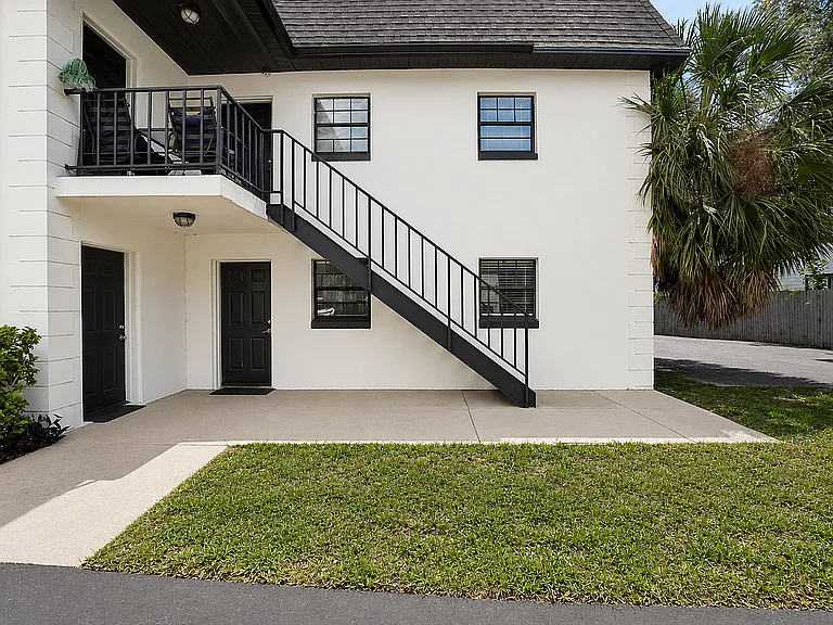 Charming duplex exterior with stylish black railings, lush landscaping, and a welcoming balcony perfect for relaxation.