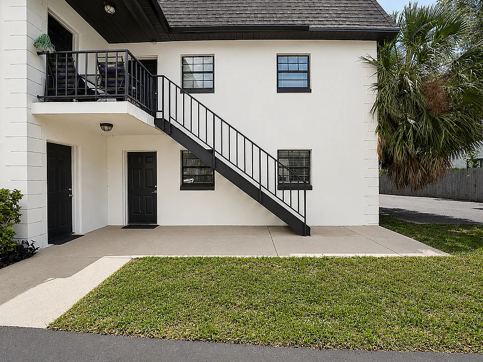 Charming duplex exterior with stylish black railings, lush landscaping, and a welcoming balcony perfect for relaxation.