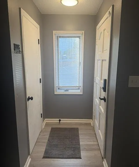 Compact entry hallway with durable flooring, window with blinds for natural light, and convenient doors for easy access.