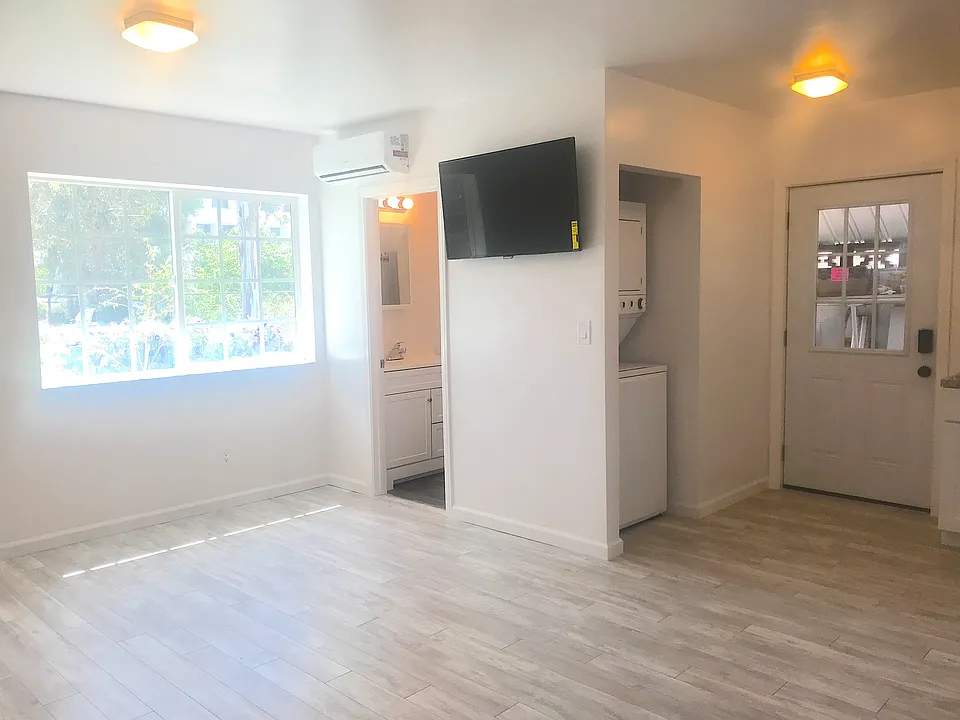 Living Room space. Includes wall-mounted TV. Window faces lush yard area.