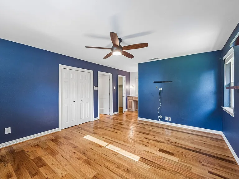 Spacious room featuring wood-finish flooring, a built-in ceiling fan with integrated lighting, and multiple windows