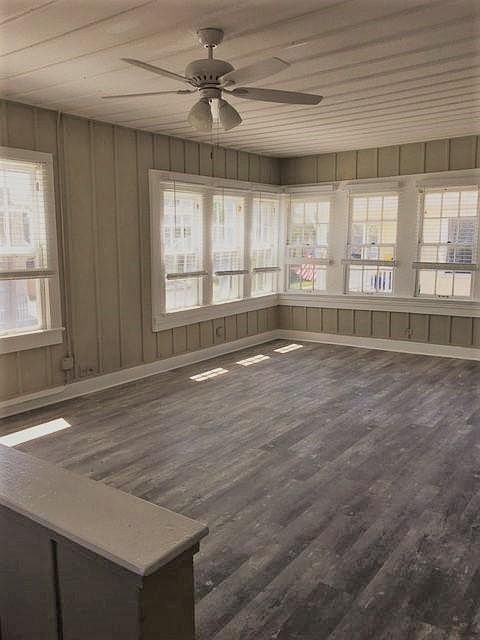 Living room with many windows and new flooring. Ceiling fan and light.