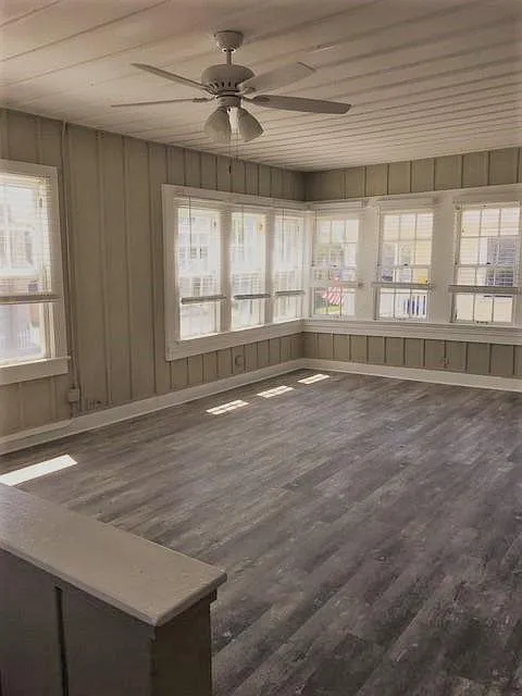 Living room with many windows and new flooring. Ceiling fan and light.