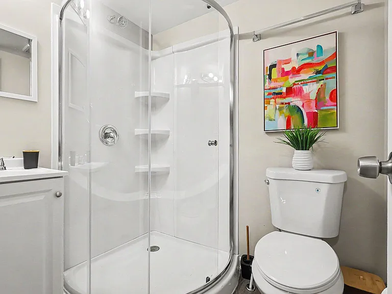 Well-kept bathroom featuring a glass-enclosed corner shower, vanity with mirror, and clean, simple finishes.