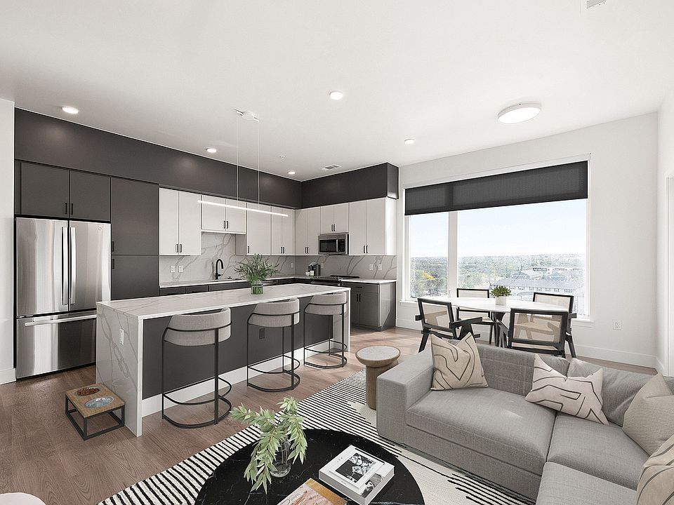 Modern open-plan kitchen and living area featuring sleek cabinetry, stainless steel appliances, a spacious island with bar seating, and stylish decor, enhanced by large windows offering scenic views.