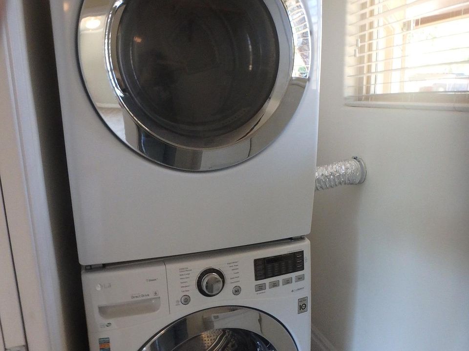 High end stacked washer and dryer plus a utility sink and hanging area in laundry room.