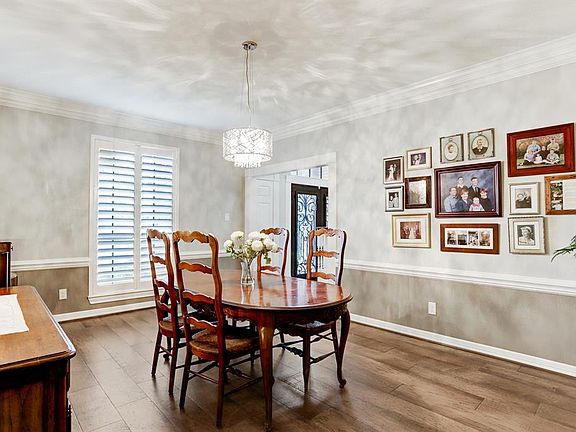Formal dining room with wood floors, plantation shutters, chair rail, stunning crown moulding, and elegant chandelier.