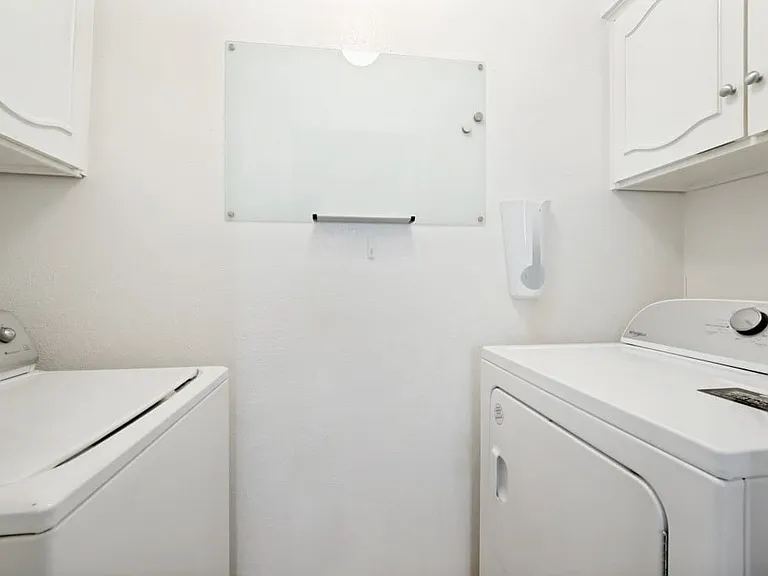 Dedicated laundry area featuring white textured walls, overhead white cabinetry with decorative arches, and brushed nickel hardware