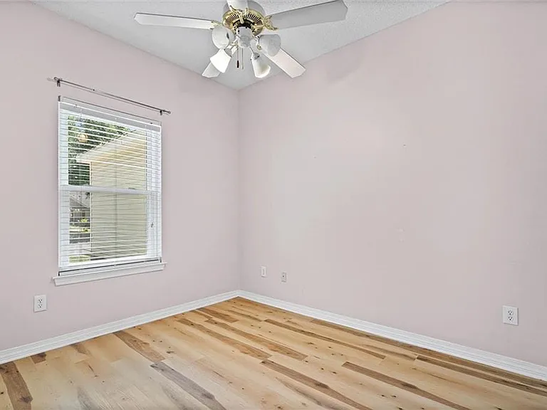 Room featuring wood-finish flooring, a ceiling fan with light fixture, and a single window with blinds