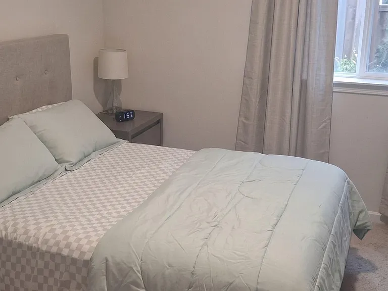 Furnished bedroom with a full-size bed, nightstand and lamp, plus a window with curtains for comfortable privacy.