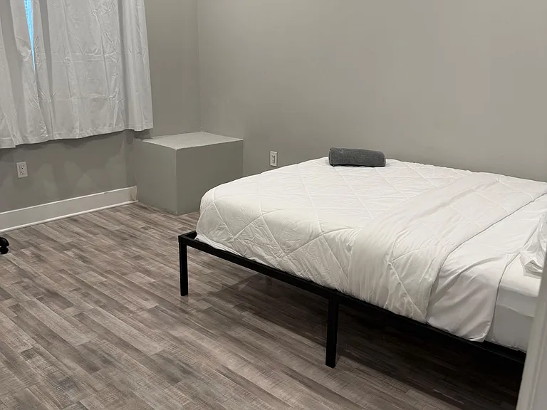 Private bedroom with a bed setup, wood-look flooring, and a window with curtains for natural light and privacy.
