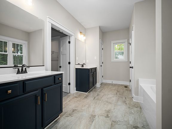 A modern bathroom with dual sinks, navy cabinetry, a large mirror, beige tiled floor, a window, and