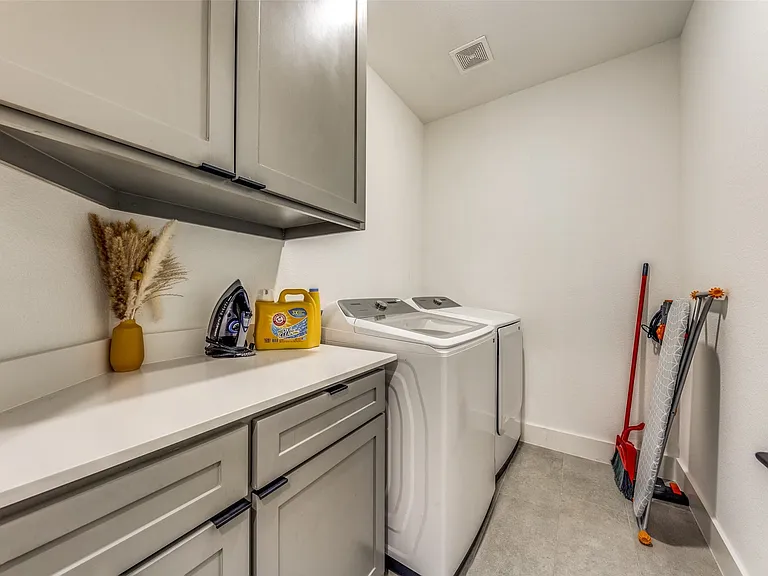 Dedicated laundry area featuring a light countertop, gray cabinetry with black hardware, and tile flooring