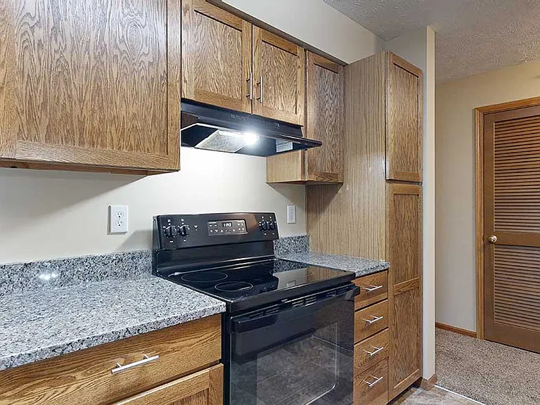 A renovated kitchen in the 1-bedroom Imperial with wooden cabinets, granite countertops, and sleek black appliances.