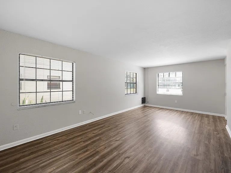 Spacious and bright living room with elegant wood flooring, large windows, and fresh neutral walls.