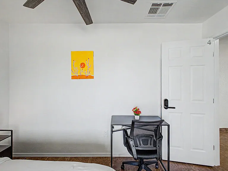 Private bedroom setup with a dedicated work desk, ceiling fan, and easy access to the adjacent hallway.