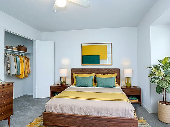 Inviting bedroom with a mid-century modern design, featuring a cozy bed with vibrant yellow and green accents, stylish wooden furniture, and an open closet space.