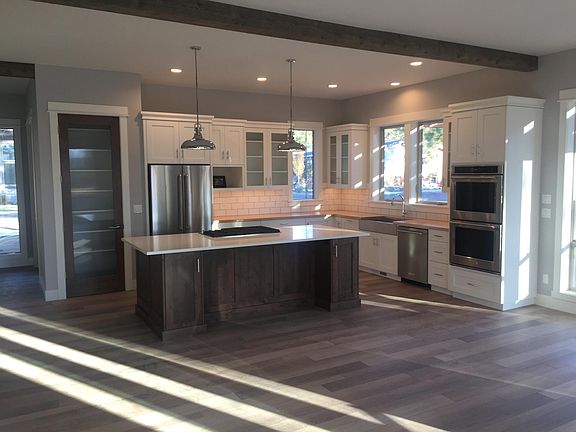 Modern kitchen with double oven, stainless steel farmhouse sink, huge island with gas cooktop. Pantry with glass door