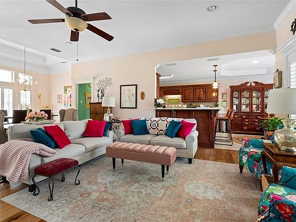 Living area featuring crown molding, light wood-type flooring, ceiling fan with notable chandelier, a raised ceiling, and visible vents