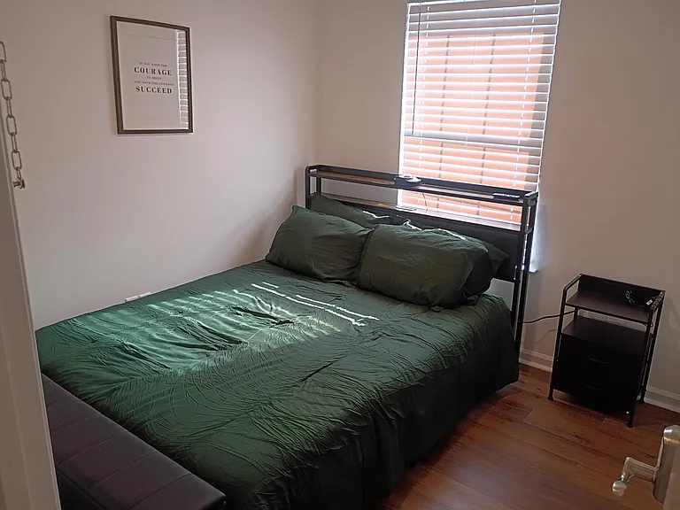 Furnished room with queen bed & nightstand charging station, ceiling fan with light, blinds for privacy and natural light.